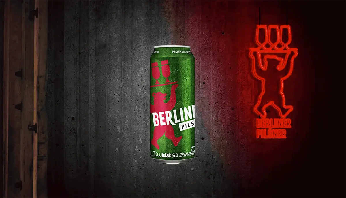 A beer can with a vibrant green label is set against a textured background with a neon sign.