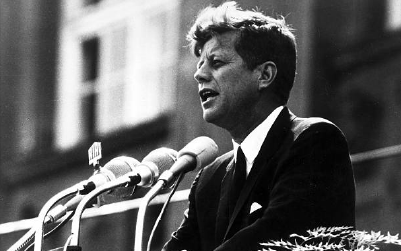 A man in a suit speaks at a podium with microphones during a public event.