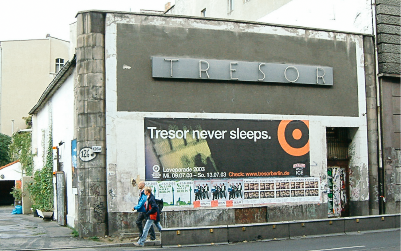 A person is walking past a large building with graffiti and posters on its walls. The words 