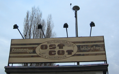 An aged billboard with faded words stands atop a structure, flanked by two security cameras.