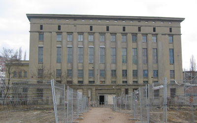 A large, formal building with many windows behind a metal fence is under renovation.