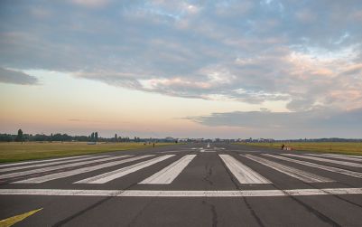 An empty runway stretches into the distance under a sky with soft sunset colors.